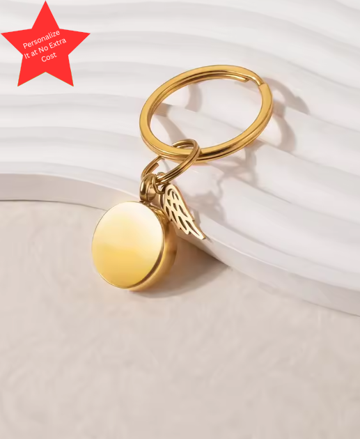 Gold cremation keychain with round memorial charm and angel wing accent, polished finish, designed to hold a small portion of ashes