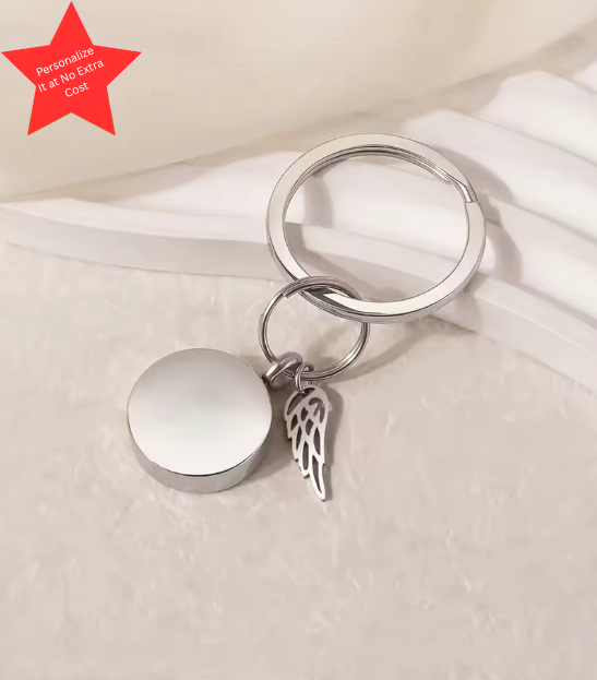 Silver cremation keychain with round memorial charm and angel wing accent, polished finish, designed to hold a small portion of ashes