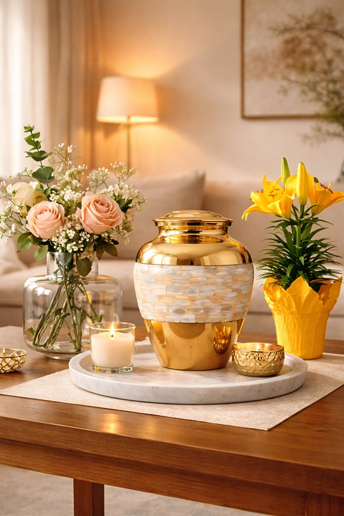 Pearl Mosaic Gold Urn with mother of pearl mosaic inlay displayed on a marble side table in a soft neutral bedroom next to a framed couple portrait — luxury adult cremation urn in polished gold finish